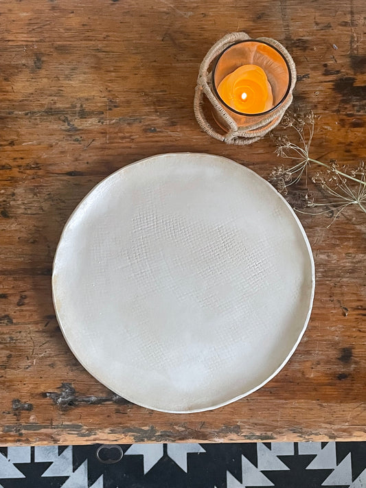 Handmade pottery dinner plate in matte white with a burlap texture.