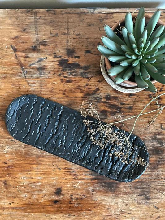 Oval ceramic tray with a tree trunk texture in a black matte glaze.